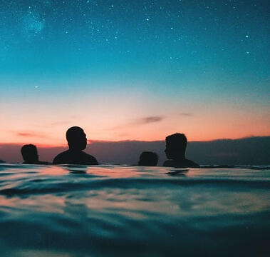 Four people standing in water, the sunset and stars behind them.