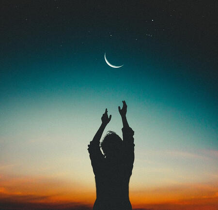 Silhouette of a person reaching for the crescent moon and stars.