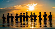 A group of people standing in water with the sunset behind them.