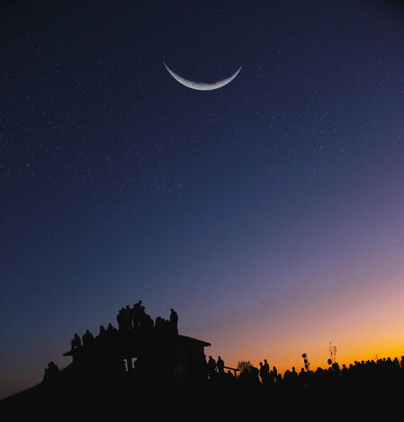 Crescent moon at night, with people silhouetted against the sky.